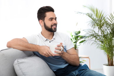 Photo of Young man with cup of drink relaxing on couch at home
