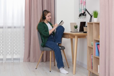 Photo of Teenage girl with headphones writing in notebook at home