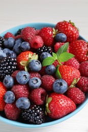 Many different fresh ripe berries in bowl on white wooden table, closeup