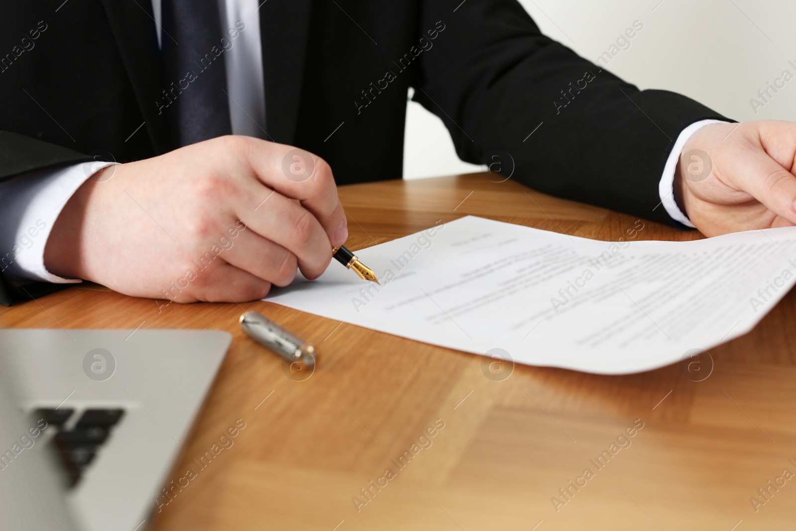 Photo of Notary signing document at wooden table, closeup