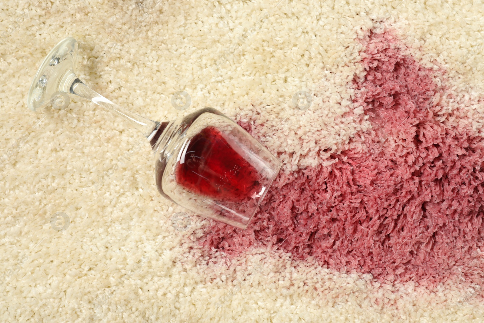 Photo of Overturned glass and spilled red wine on beige carpet, top view