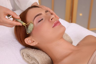 Young woman receiving facial massage with jade roller in beauty salon, closeup