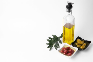 Photo of Bottle of cooking oil, olives and leaves on white background. Space for text