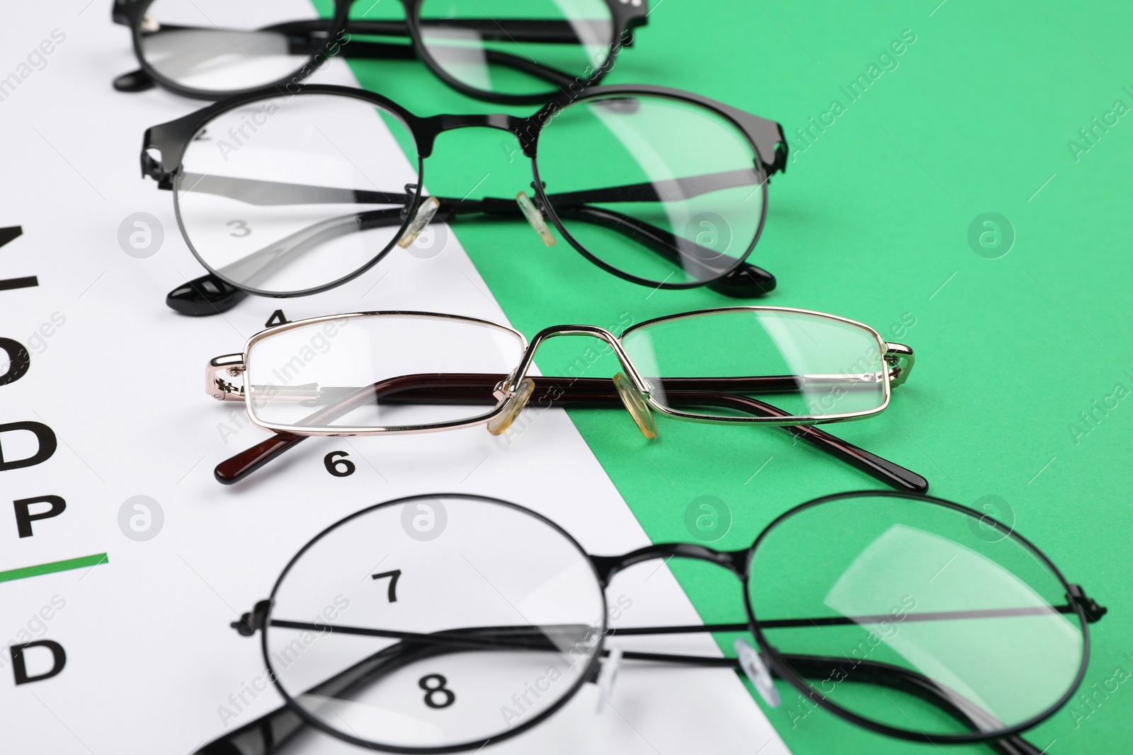 Photo of Vision test chart and glasses on green background, closeup