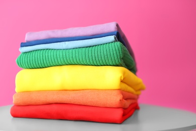 Photo of Stack of rainbow clothes on table against color background