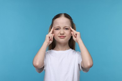 Photo of Little girl suffering from headache on light blue background