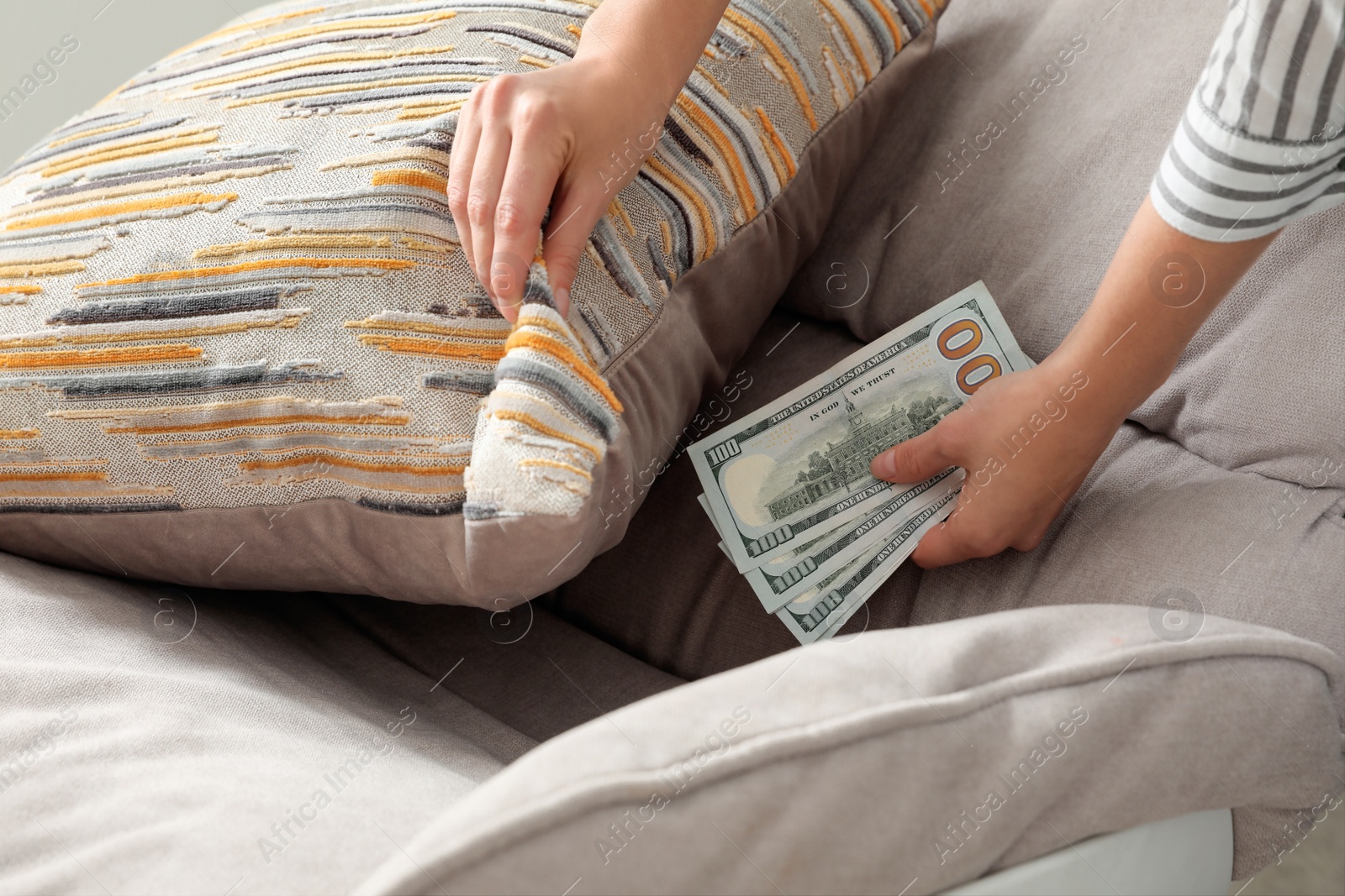 Photo of Woman hiding dollar banknotes under pillow on armchair indoors, closeup. Money savings