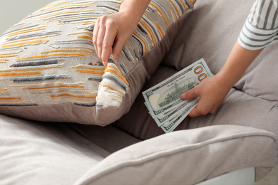 Photo of Woman hiding dollar banknotes under pillow on armchair indoors, closeup. Money savings