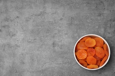 Photo of Bowl of dried apricots on grey background, top view with space for text. Healthy fruit