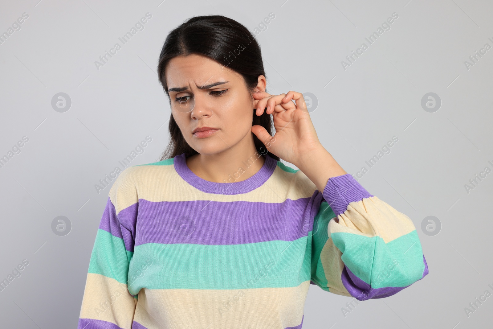 Photo of Young woman suffering from ear pain on light grey background