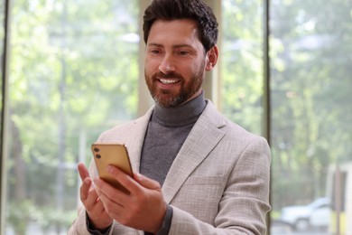 Photo of Positive handsome man using his smartphone indoors