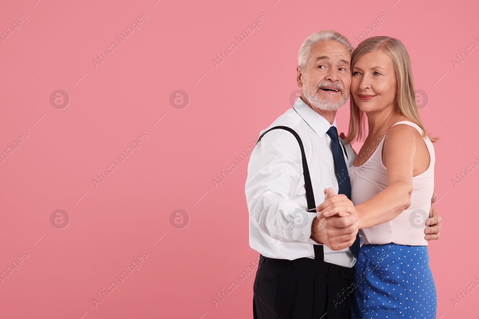 Photo of Senior couple dancing together on pink background, space for text