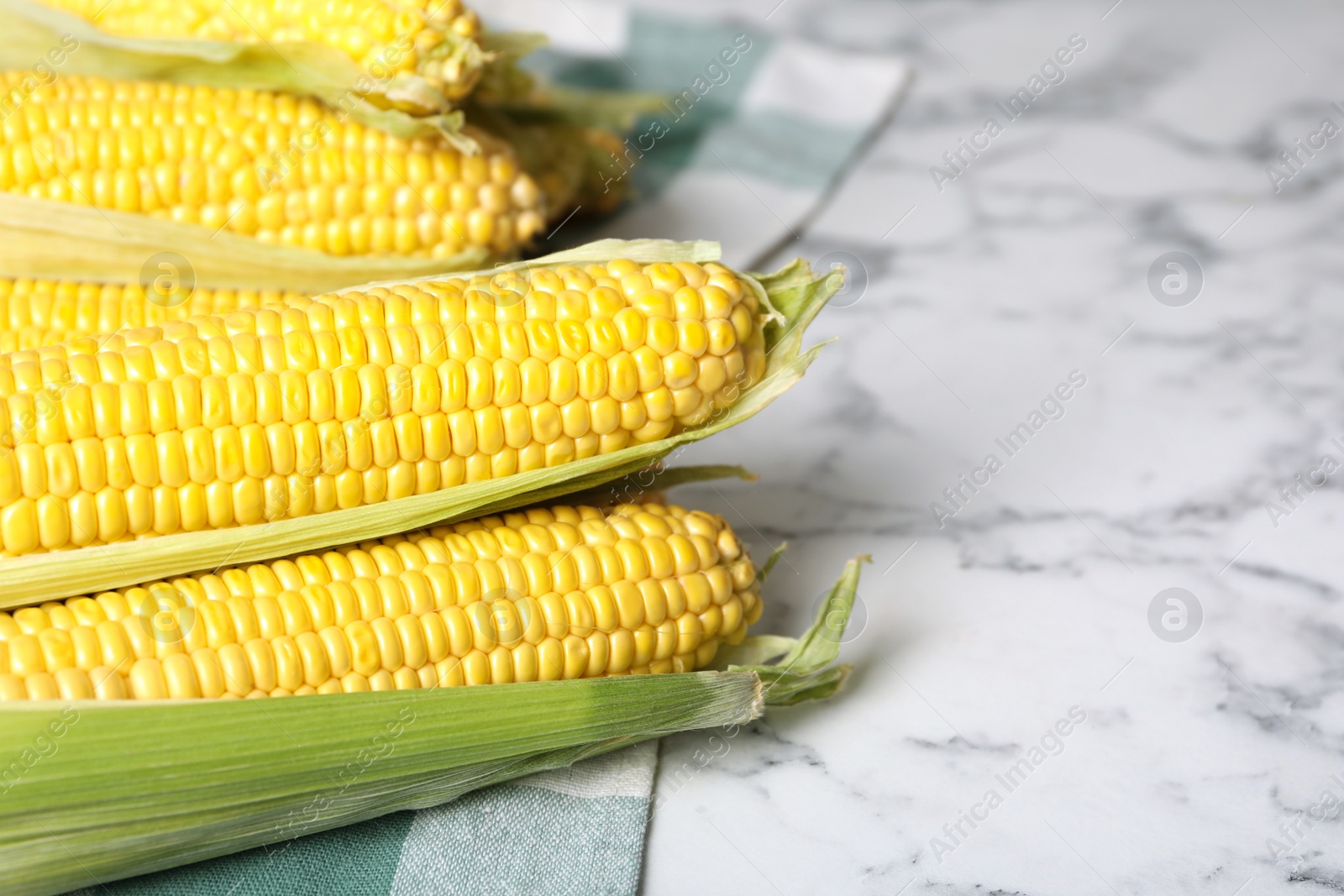 Photo of Bunch of corn cobs on white marble table, closeup