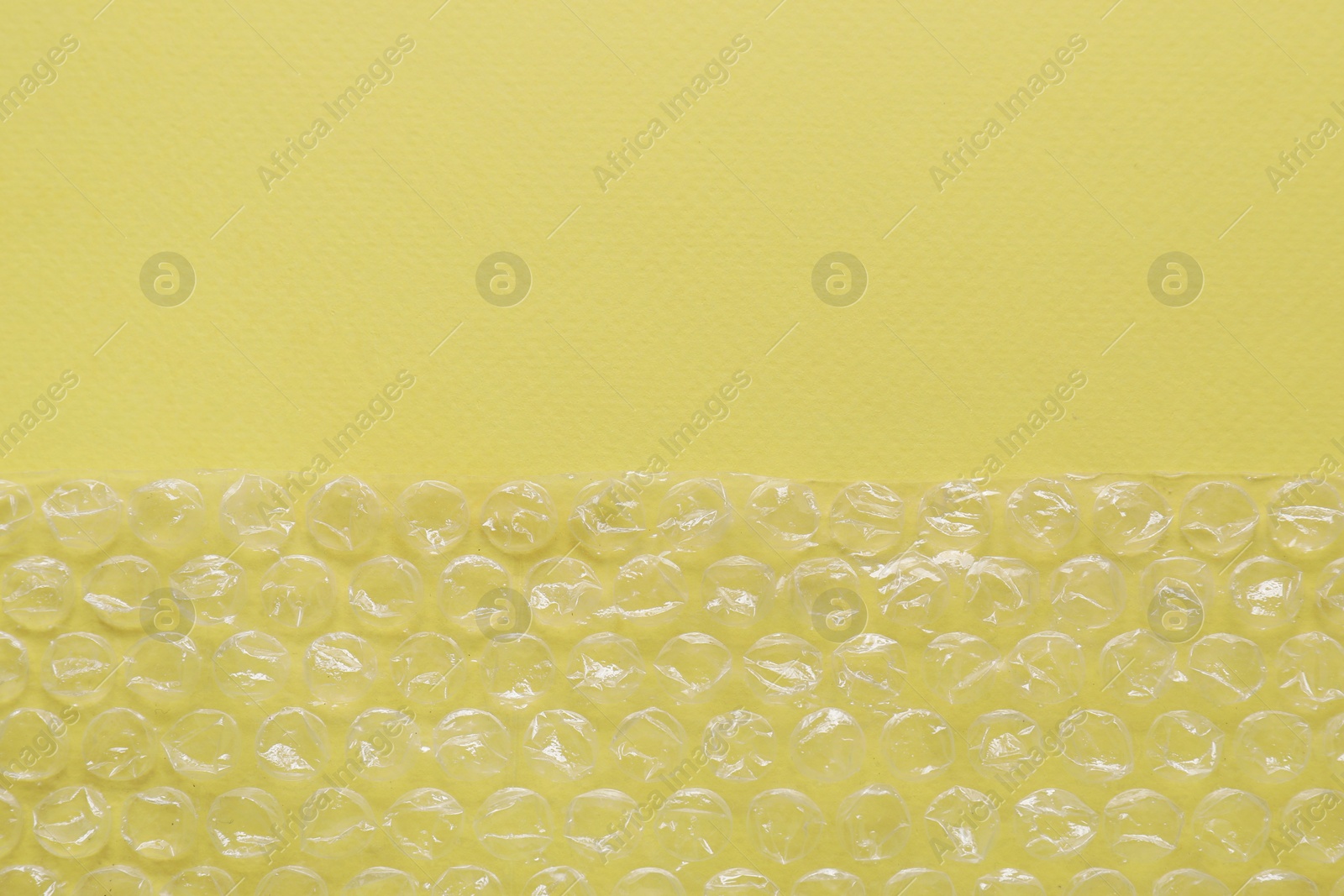 Photo of Transparent bubble wrap on yellow background, top view. Space for text