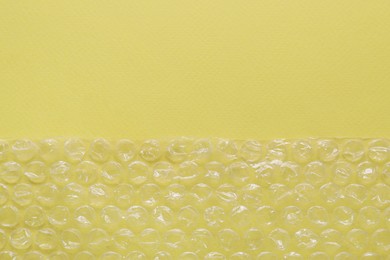 Photo of Transparent bubble wrap on yellow background, top view. Space for text