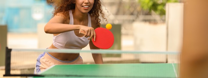 Image of African-American woman playing ping pong with friend outdoors. Banner design