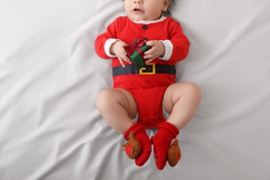 Baby wearing festive Christmas costume with gift box on white bedsheet, top view