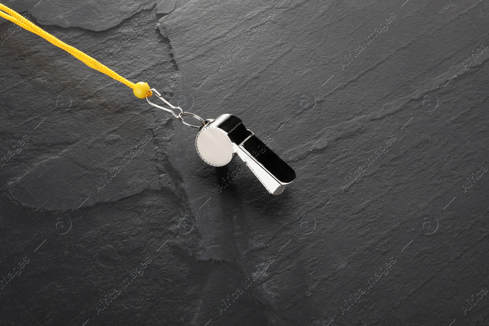 Photo of Referee equipment. Metal whistle on black textured background, closeup and space for text