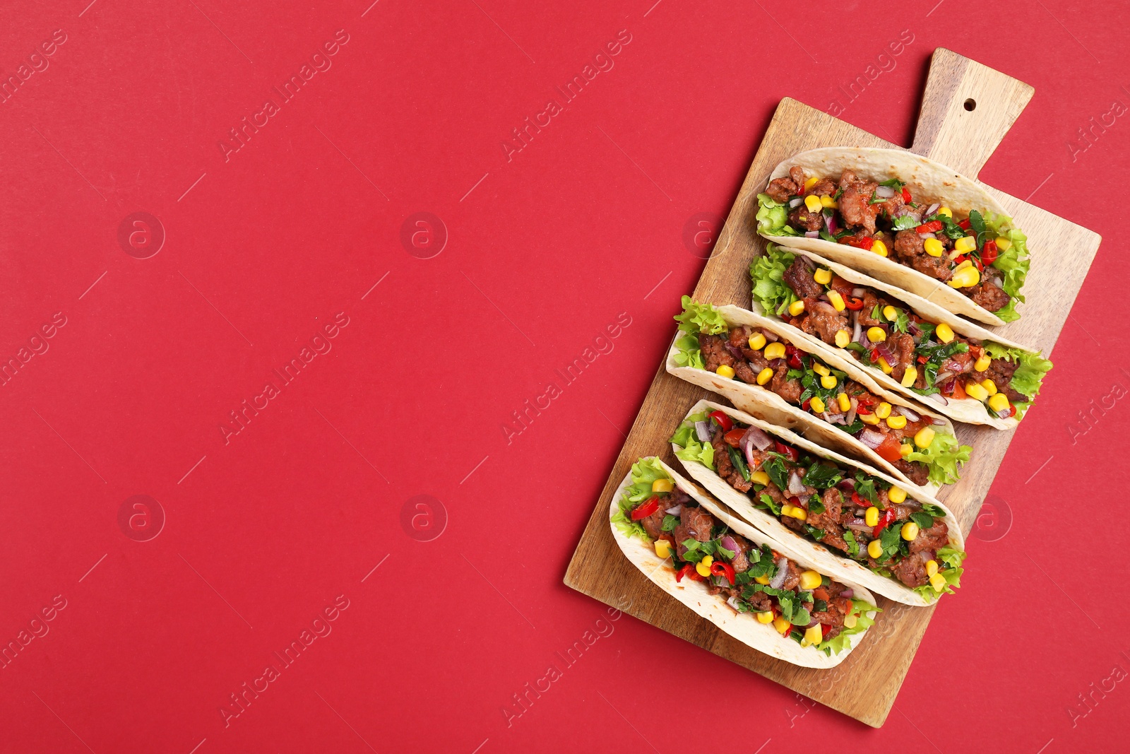 Photo of Delicious tacos with meat and vegetables on red table, top view. Space for text