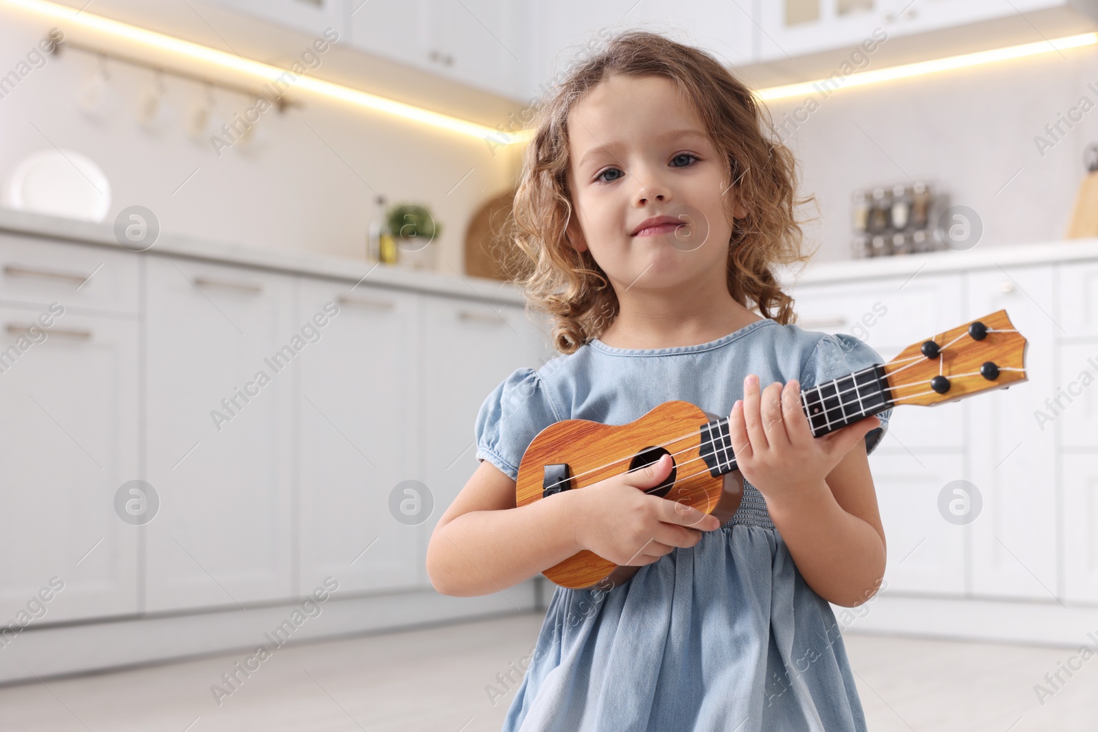 Photo of Little girl playing toy guitar in kitchen. Space for text