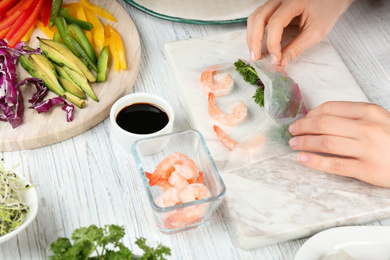 Photo of Woman making rice paper roll at white wooden table, closeup