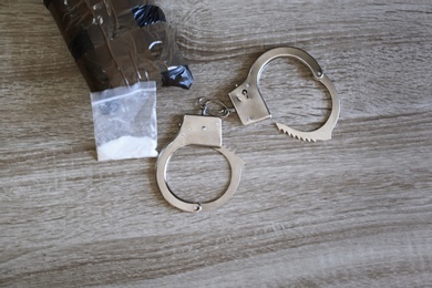 Drugs with handcuffs on wooden background, above view. Criminal law