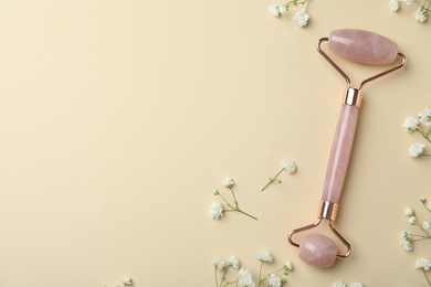 Natural face roller and flowers on beige background, flat lay. Space for text