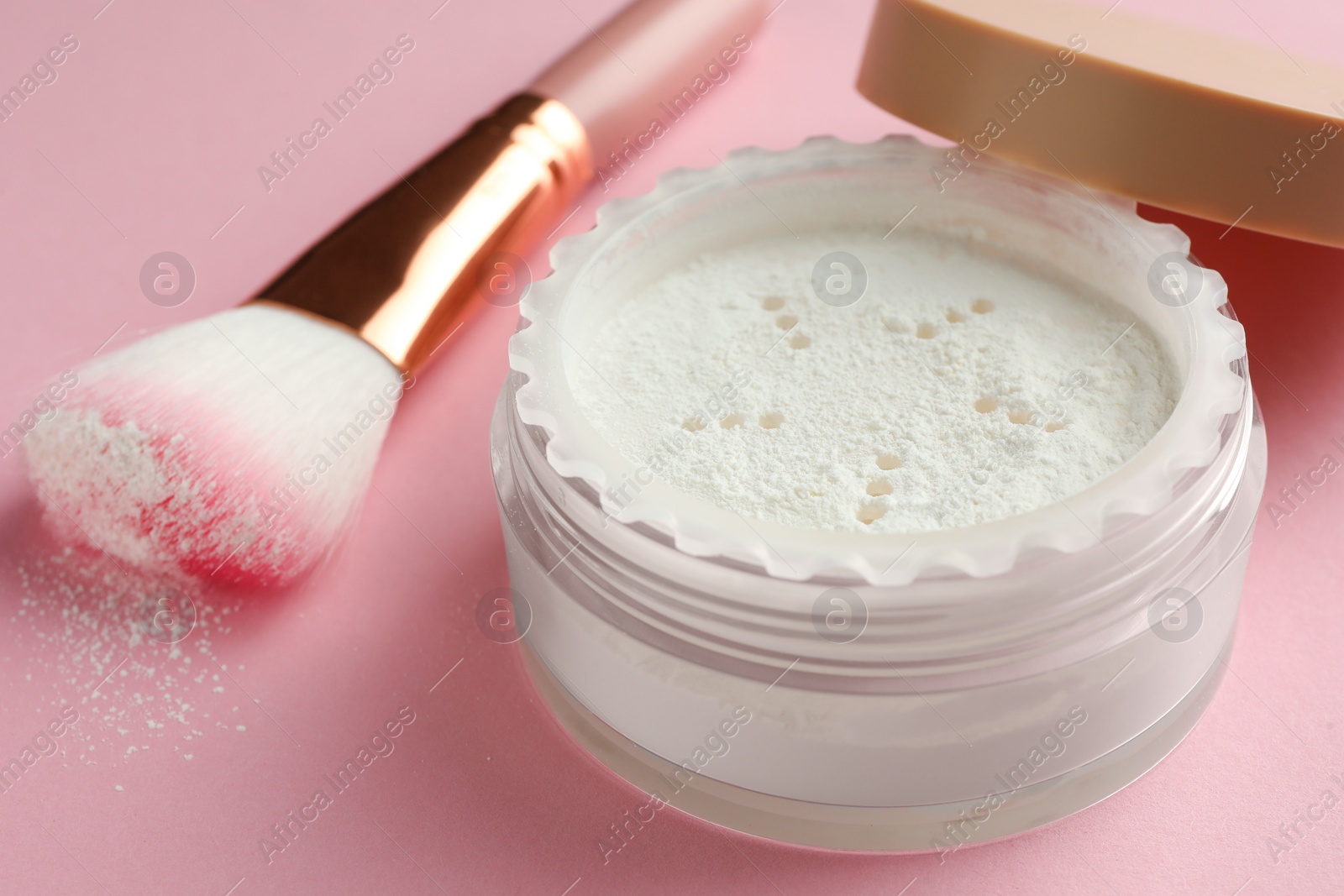 Photo of Rice loose face powder and makeup brush on pink background, closeup