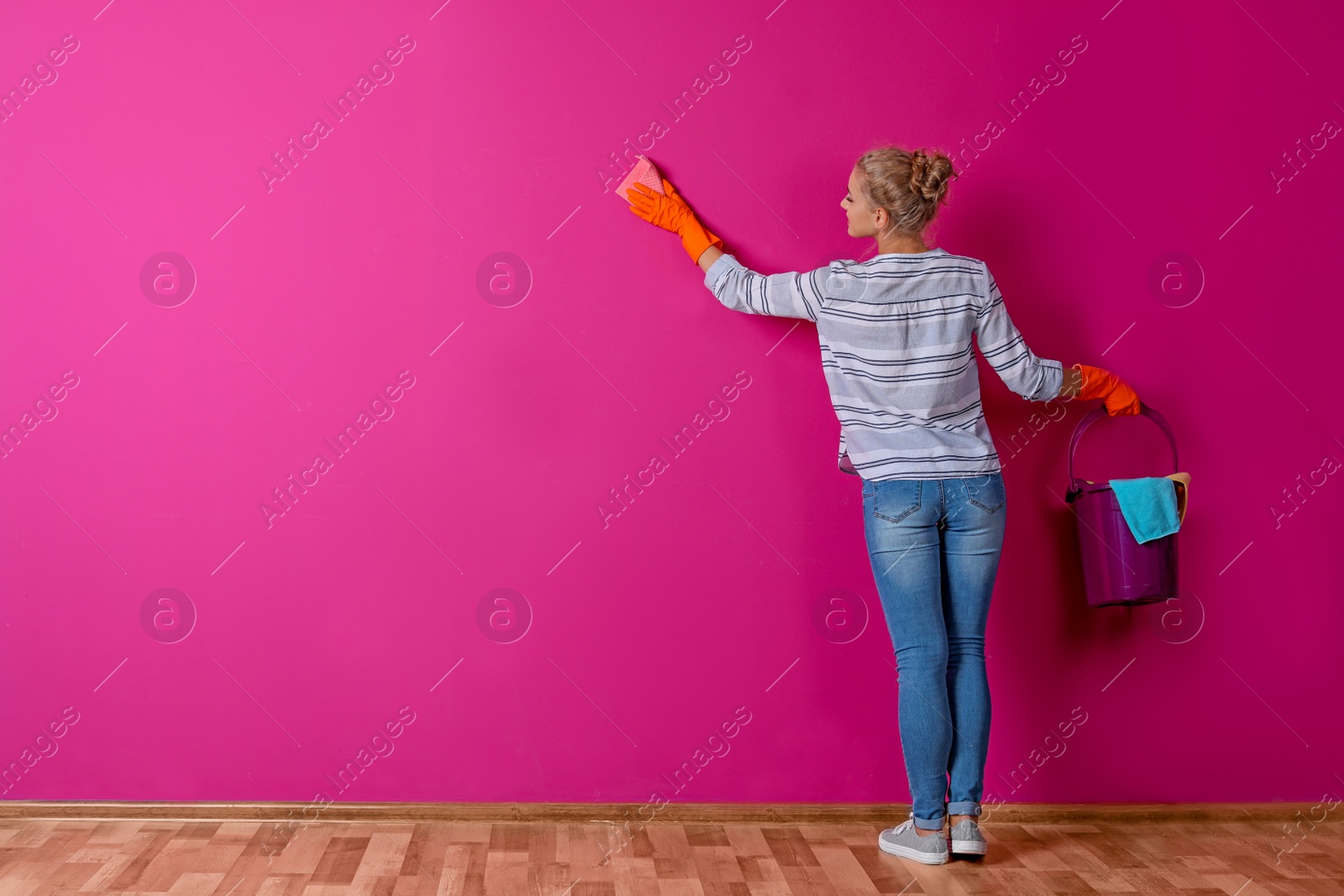 Photo of Woman in gloves cleaning color wall with rag