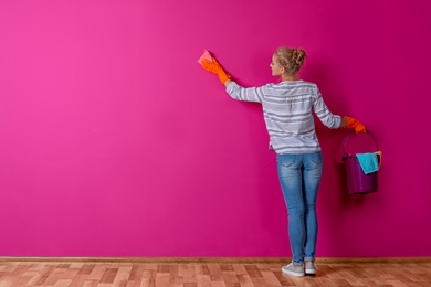 Photo of Woman in gloves cleaning color wall with rag