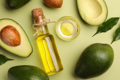 Cooking oil and fresh avocados on light green background, flat lay