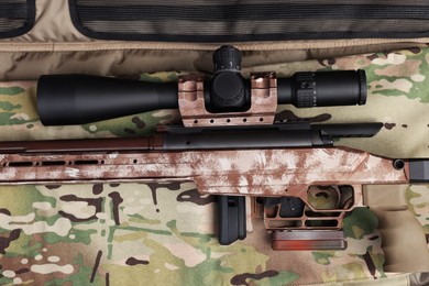 Photo of Modern powerful sniper rifle with telescopic sight on camouflage fabric, top view