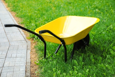 Photo of Yellow wheelbarrow on green grass outdoors. Gardening tool