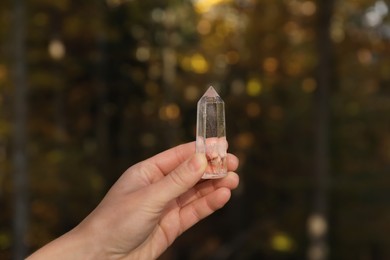 Photo of Woman holding clear quartz crystal outdoors, closeup
