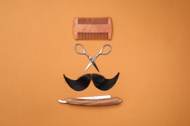 Photo of Artificial moustache and barber tools on orange background, flat lay
