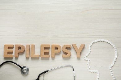 Photo of Human head silhouette made of pills, word Epilepsy and stethoscope on white wooden table, flat lay. Space for text