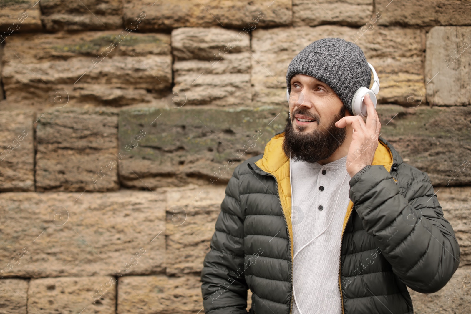 Photo of Mature man with headphones listening to music near stone wall. Space for text