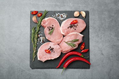 Photo of Pieces of raw pork meat, chili peppers and spices on grey table, top view