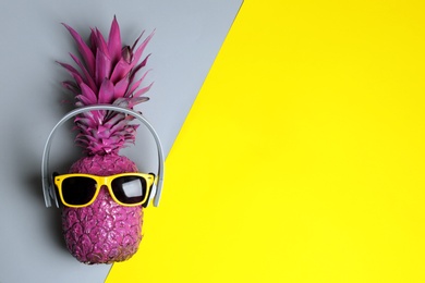 Pineapple with headphones and sunglasses on color background, top view with space for text