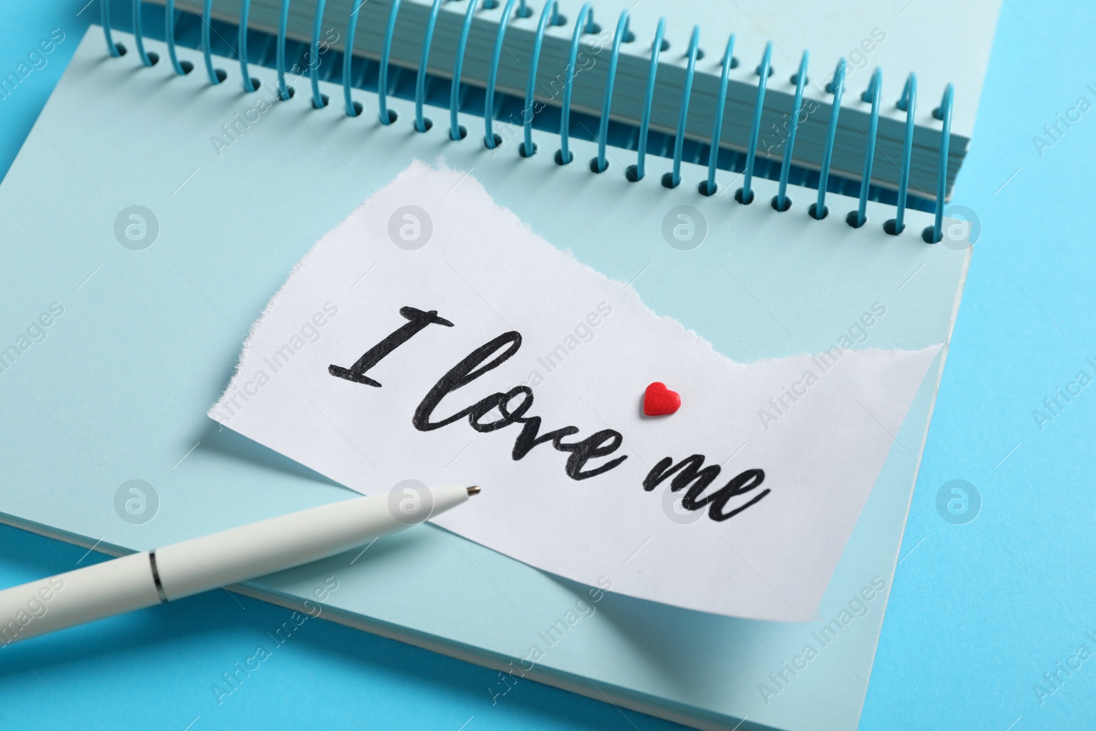 Photo of Paper with handwritten phrase I Love Me, notebook and pen on light blue background, closeup