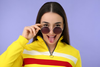 Happy woman in sunglasses showing her tongue on violet background