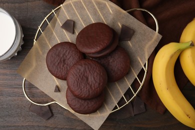 Photo of Delicious choco pies, bananas and glass of milk on wooden table, flat lay