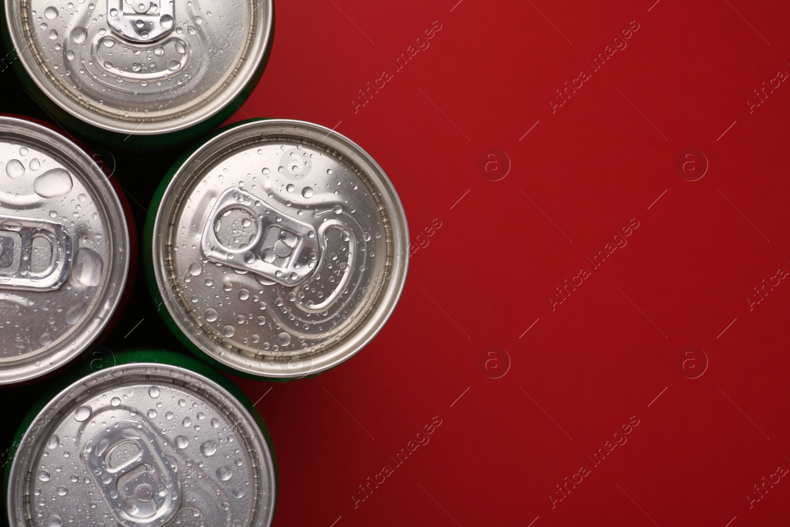 Photo of Energy drinks in wet cans on red background, top view. Space for text