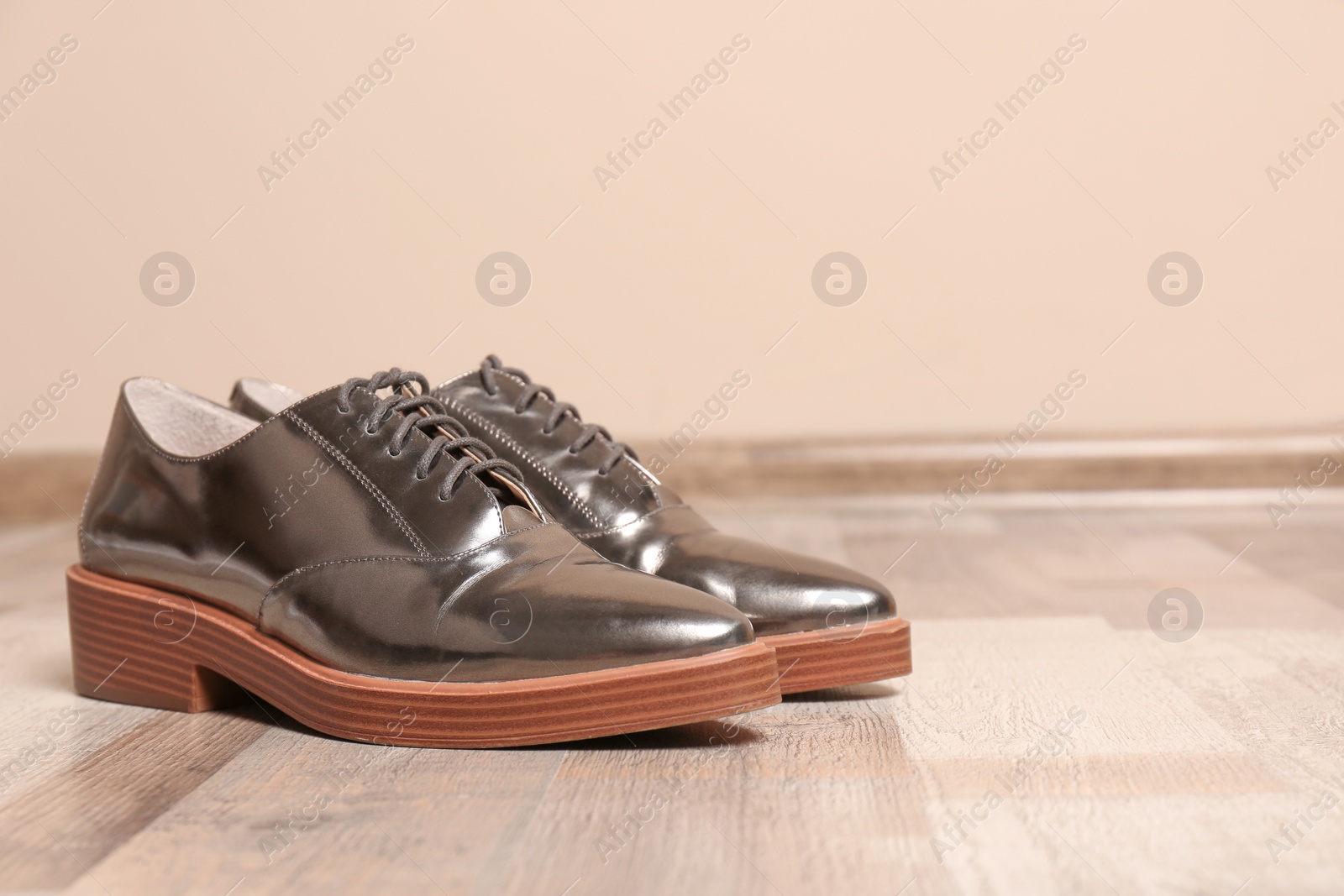 Photo of Pair of elegant shoes on floor near color wall, space for text