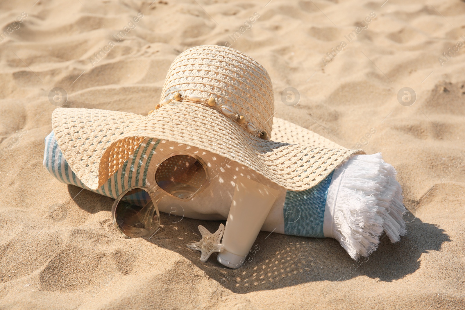 Photo of Straw hat, towel, sunscreen, starfish and sunglasses on sand