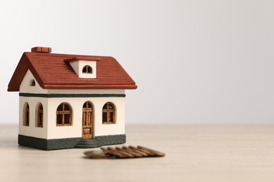 Mortgage concept. House model and coins on wooden table against white background, space for text