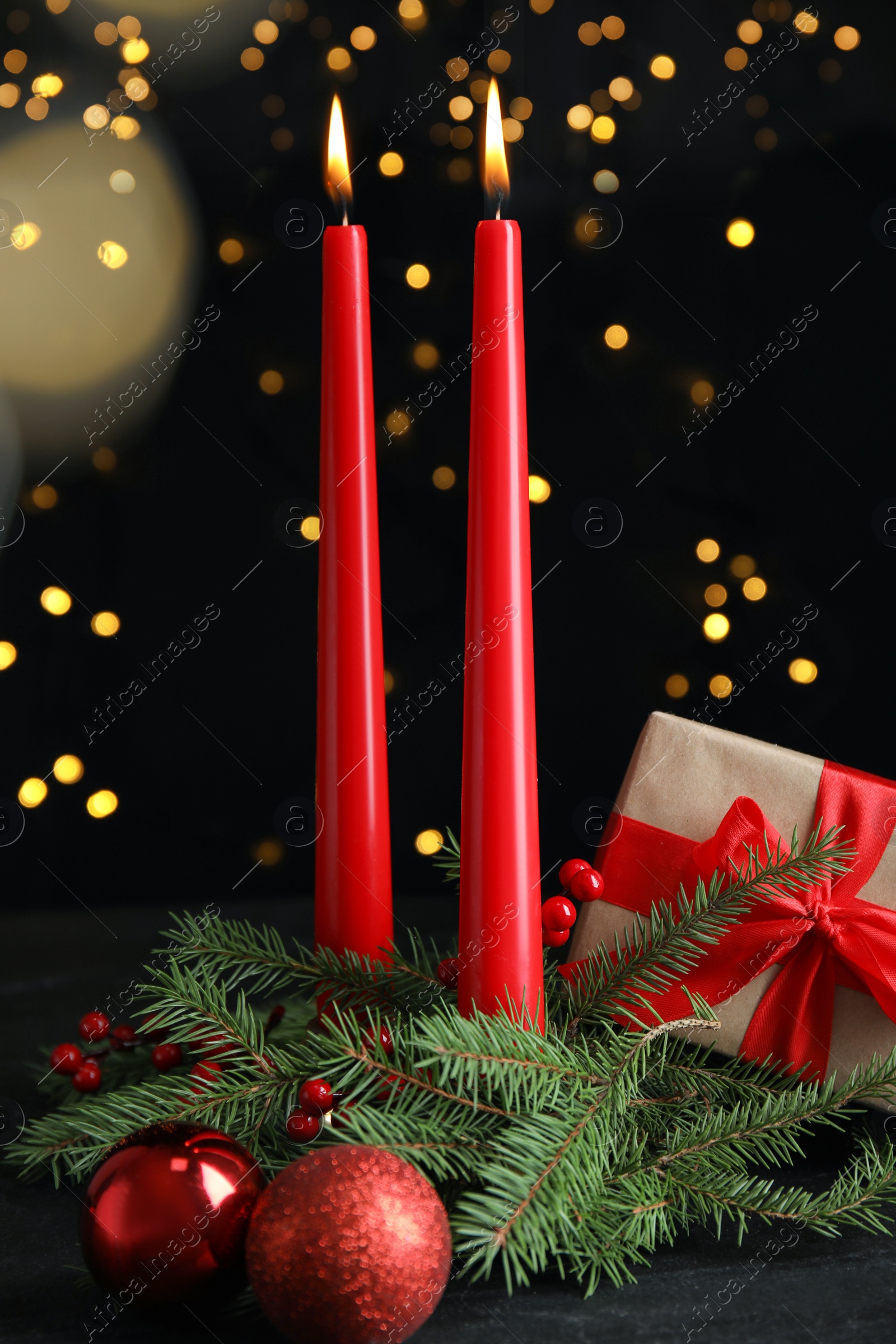 Photo of Burning candles, gift box and decor on dark table against blurred festive lights. Christmas eve