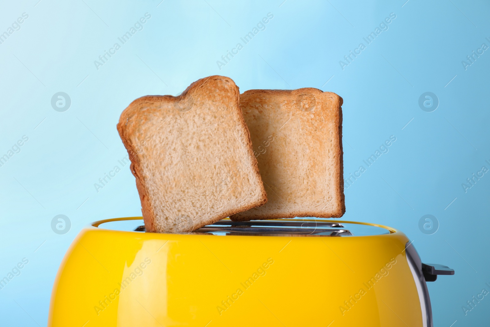 Photo of Yellow toaster with roasted bread against light blue background, closeup