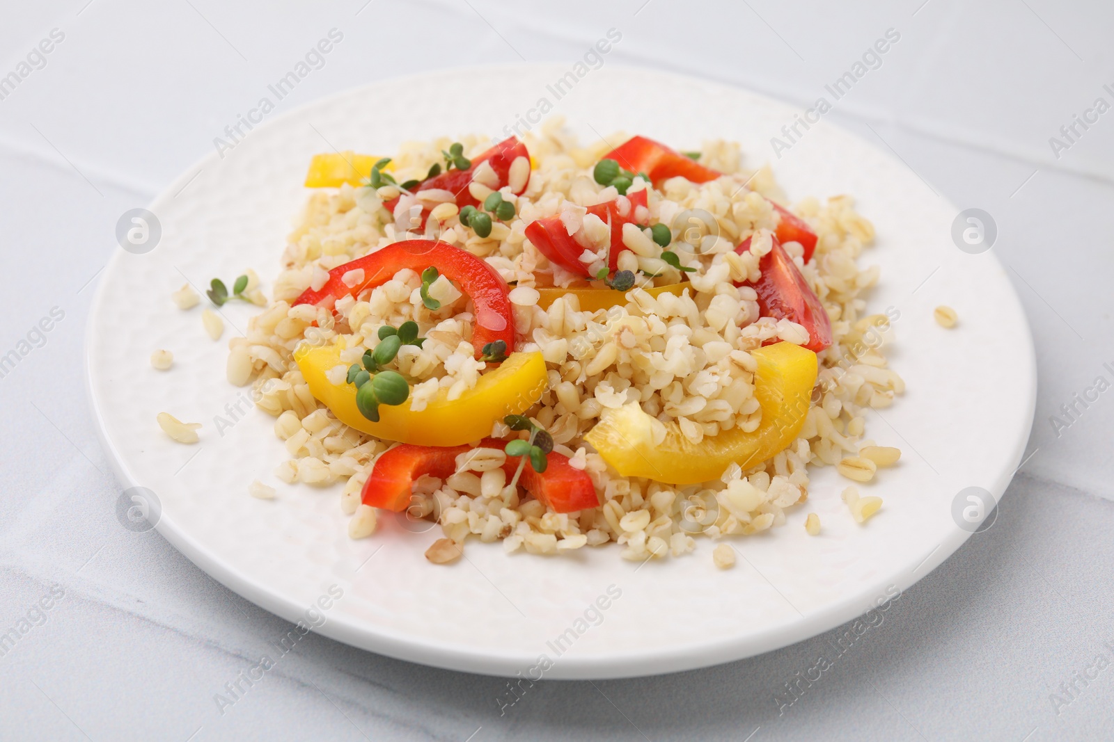 Photo of Plate of cooked bulgur with vegetables on white tiled table
