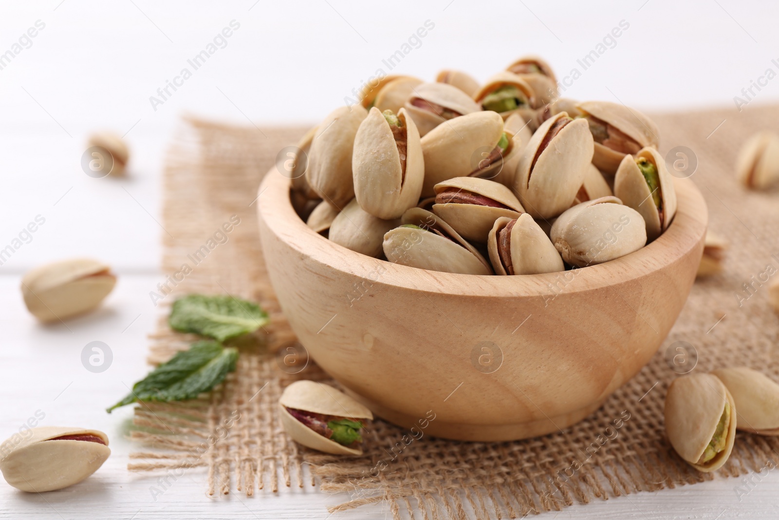 Photo of Tasty pistachios in bowl on white wooden table, closeup